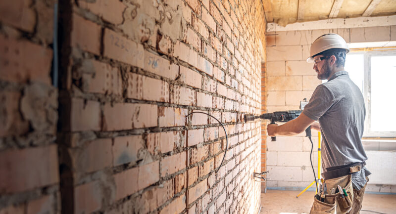 Bauarbeiter bearbeitet Ziegelwand mit Bohrmschine